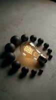 Illuminated vintage filament bulb surrounded by black spheres on concrete surface, symbolizing innovation and creative thinking for business concepts.