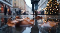 Autumn leaves in puddle reflection on rainy city street with blurred pedestrian and festive holiday lights creating atmospheric urban scene at dusk.