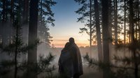 Person in hooded cloak standing in misty forest at sunrise, surrounded by tall evergreen trees and fog, contemplative outdoor scene.
