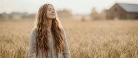 Young woman with long wavy hair enjoying peaceful moment in golden wheat field at sunset, eyes closed in serene contemplation for wellness and mindfulness content.