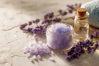 Lavender spa treatment with purple bath salts, essential oil bottle, towel and dried lavender flowers on rustic wooden background for relaxation and wellness.