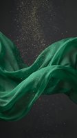 Flowing emerald silk fabric with golden glitter particles dispersing against dark background, creating elegant wave motion for luxury design and premium branding projects.