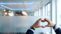 Business professional making heart shape with hands in modern office environment expressing love care and positive workplace culture.