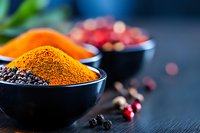 Vibrant orange turmeric powder and black peppercorns in dark ceramic bowls against moody background with scattered cranberries, macro food photography.