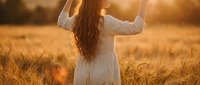 Young woman with long hair celebrating in golden wheat field at sunset with arms raised in victory pose expressing joy and freedom.