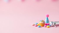 Birthday cupcake with colorful sprinkles, party hat and confetti on pink background with copy space for celebration design.
