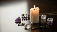 Mystical altar setup with burning candle, amethyst crystals, pentagram symbol, and lavender sprigs for spiritual rituals and meditation practices.