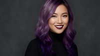 Young Asian woman with vibrant purple hair smiling confidently in black turtleneck against dark background for beauty and fashion campaigns.