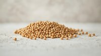 Raw yellow mustard seeds scattered on light textured surface, macro food photography with selective focus and natural lighting for culinary designs.