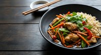 Asian stir-fry with beef, vegetables and noodles in black pan on wooden table with chopsticks and soy sauce for restaurant menu and cooking content.