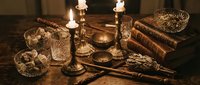 Vintage study desk arrangement with lit candelabra, crystal glasses, leather-bound books, and antique writing instruments on dark wooden surface, evoking classic literature and scholarly atmosphere.