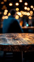 Man in blue shirt sitting at wooden table in bar with warm bokeh lights, suitable for hospitality, lifestyle, and evening ambiance concepts.