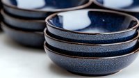 Handcrafted ceramic bowls in deep navy blue with speckled glaze and bronze rim stacked together, showing artisanal craftsmanship and rustic elegance. For food styling.
