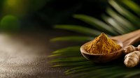 Ground turmeric powder in wooden spoon with fresh root and palm leaves on dark background, aromatic spice for healthy cooking and wellness recipes.