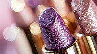 Luxurious purple metallic lipstick with glitter sparkle effect on blurred background. Close up macro shot shows shimmering texture for cosmetic and beauty.