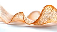 Crisp potato chips arranged in elegant wavy curves creating abstract composition with soft shadows on white background, macro food photography.