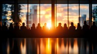 Business team silhouettes against sunset city skyline through office windows with golden light reflection on conference table for corporate meetings.