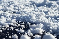 Macro shot of crystalline snow texture on dark surface showing detailed ice crystals and snowflakes in winter weather conditions with soft bokeh effect.