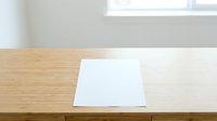 Blank white paper sheet on wooden desk with natural window light, ready for mockup, branding, or design projects.