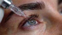 Closeup of cosmetic procedure with syringe near eye area, showing detailed view of skin texture and eyebrow during beauty treatment.