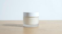 White cosmetic jar with silver lid on wooden surface against neutral background for skincare and beauty product packaging design.