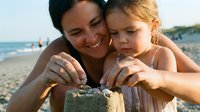 Mother and young daughter building sandcastle together on sunny beach, enjoying summer vacation and quality family time by the ocean.