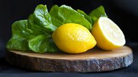Fresh organic lemons with green leaves on rustic wooden cutting board for healthy cooking and natural ingredients in kitchen preparation.