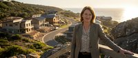 Woman in business casual attire standing on a clifftop overlooking luxury coastal homes and ocean views. Suitable for real estate, lifestyle, and professional business concepts.
