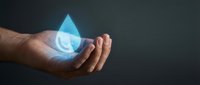 Male hand holding glowing water droplet symbol against dark background, representing conservation, sustainability, environmental protection and clean water resources.