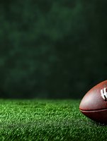 American football on green artificial turf field with dark background and copy space for sports marketing and game day promotions.