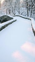 Snow-covered stone bridge pathway through winter forest with bare trees and soft pink light creating peaceful seasonal landscape for holiday greeting cards.