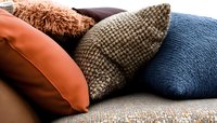 Decorative throw pillows in orange, brown, blue and textured fabrics arranged on gray sofa, creating cozy home atmosphere for interior design styling.