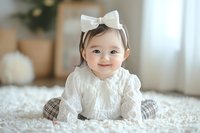 Smiling baby in white lace dress with bow headband sitting on fluffy carpet in cozy home setting with soft natural light and minimal decor.