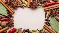 Aromatic spices frame creating copy space with cinnamon sticks, star anise, bay leaves, cardamom pods and chili peppers on neutral background for culinary designs.