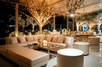 Luxurious wedding reception lounge area with illuminated trees, cream sectional seating, and modern decor creates elegant atmosphere for evening celebration.