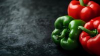 Fresh red and green bell peppers on dark slate surface for cooking and healthy eating recipes.
