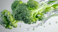Fresh green broccoli florets with water drops splashing in clear liquid, macro view on light background showing vegetable freshness and hydration.