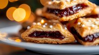Flaky pastries filled with dark berry jam on white plate against blurred golden bokeh lights, sprinkled with sugar crystals, close-up view of homemade dessert.