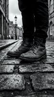 Close-up of worn lace-up boots on cobblestone street in urban setting. Low-angle perspective captures weathered footwear and historic architecture for lifestyle and travel concepts.