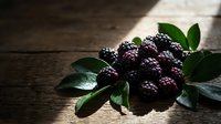 Ripe blackberries with fresh green leaves on rustic wooden surface, ideal for food and beverage marketing, recipe blogs, and culinary content.