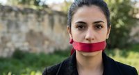 Young Middle Eastern businesswoman with red tape over mouth symbolizing censorship and silenced voice in professional setting.