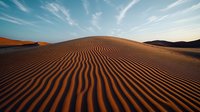 Golden sand dunes with distinct ripple patterns stretching to horizon under dramatic cirrus clouds in desert landscape at sunset, natural abstract formation.