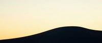 Silhouette of rolling hills against warm golden sunset sky, creating minimalist landscape with soft gradient horizon for backgrounds and design projects.