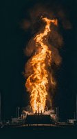 Massive flame eruption shooting upward from industrial platform at night, with sparks dispersing against dark sky. Suitable for energy, power, danger, and industrial design projects.