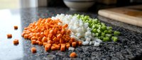 Fresh diced vegetables on granite counter including orange carrots, white onions and green celery ready for cooking and meal preparation in modern kitchen.