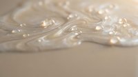 Luxurious white cream with water droplets swirling on a beige surface, evoking skincare, beauty, and cosmetic product concepts.