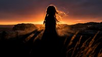 Woman silhouette with flowing hair standing on rocky terrain against dramatic fiery sunset sky, conveying freedom and solitude.