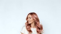 Young woman with long wavy rose gold hair wearing white shirt, smiling with eyes closed against neutral background, suitable for beauty and lifestyle content.