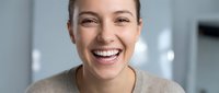 Happy young Caucasian woman with bright smile laughing joyfully in modern office environment. Professional headshot for business and lifestyle content.