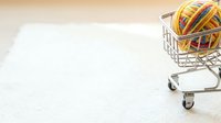 Shopping cart filled with colorful yarn balls on white surface, representing craft supplies, hobbies, and online shopping for knitting and crochet materials.